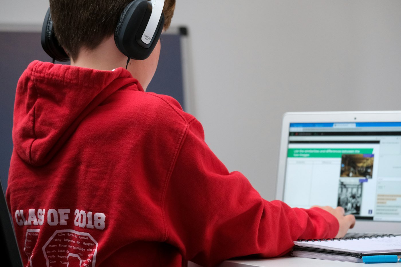 Boy in red hoodie wearing headphones, focused on a project