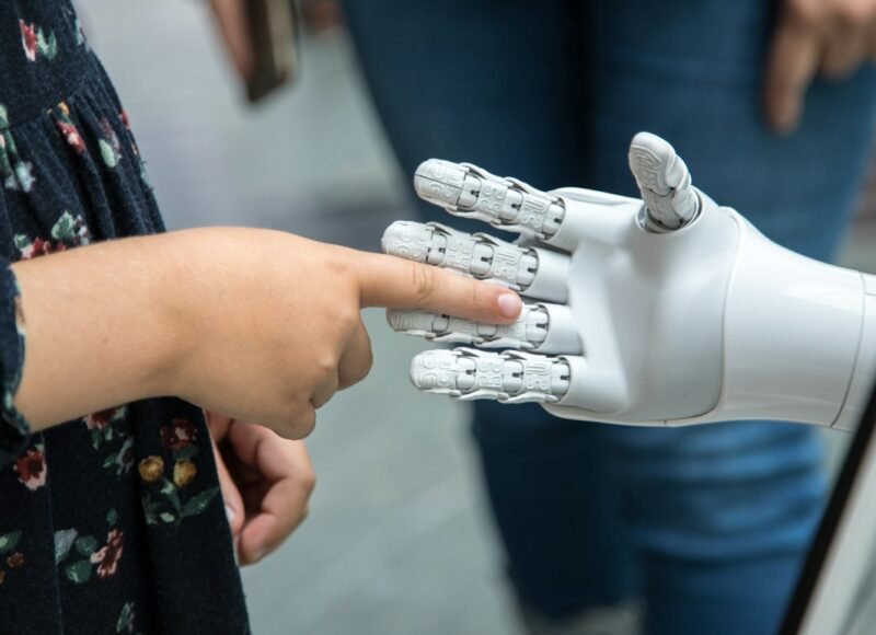 Child touching the finger of a white robotic hand, representing AI and children