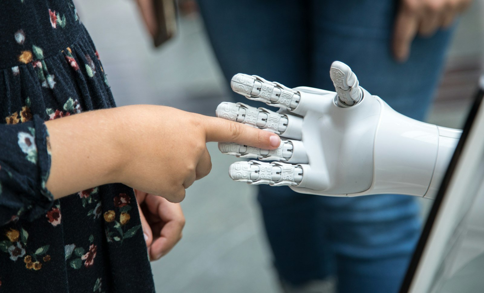 Child touching the finger of a white robotic hand, representing AI and children