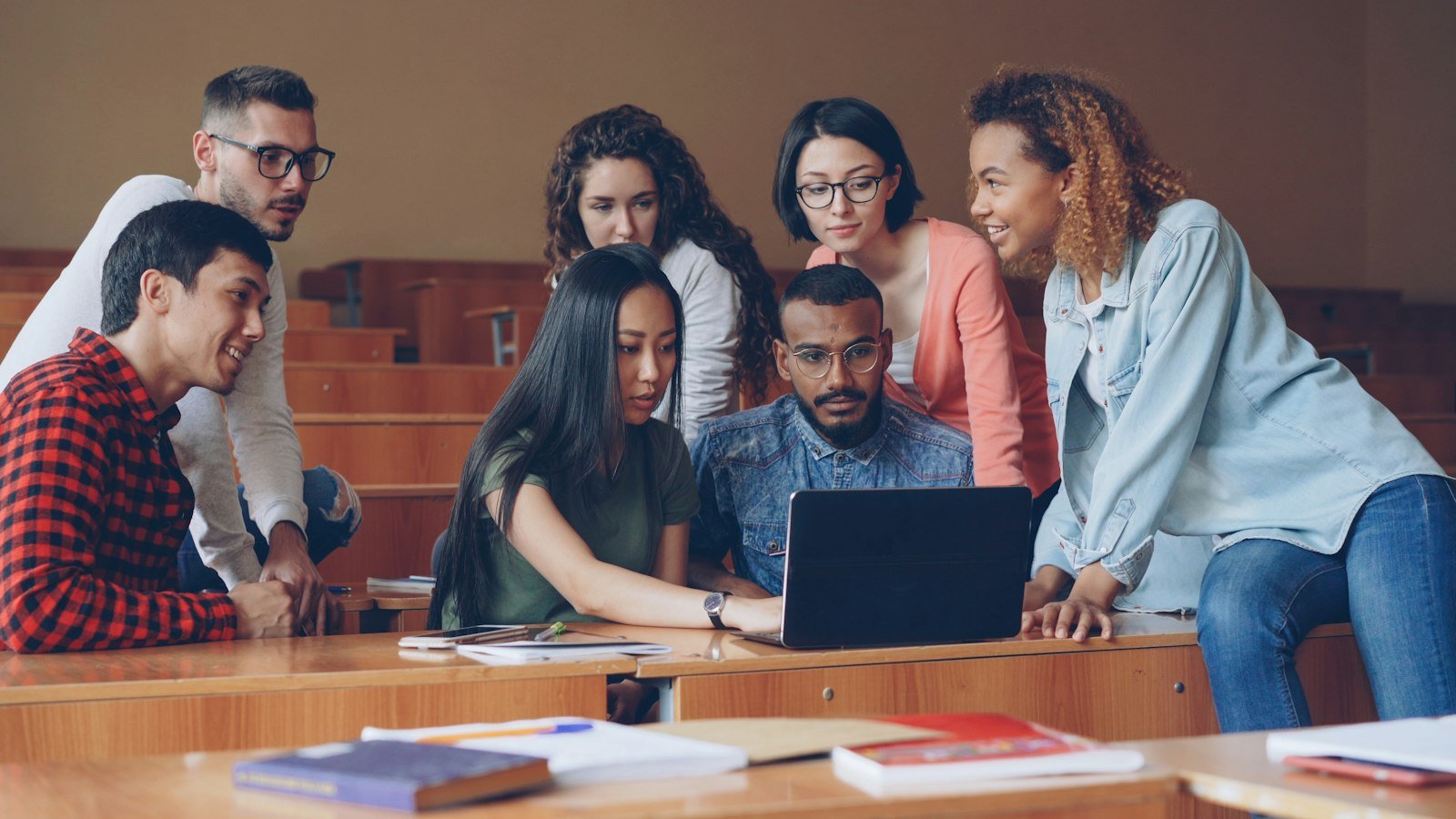 Diverse group of students gathered around a laptop in a school setting