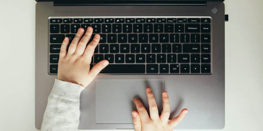 Close-up of a child's hands typing on a laptop keyboard