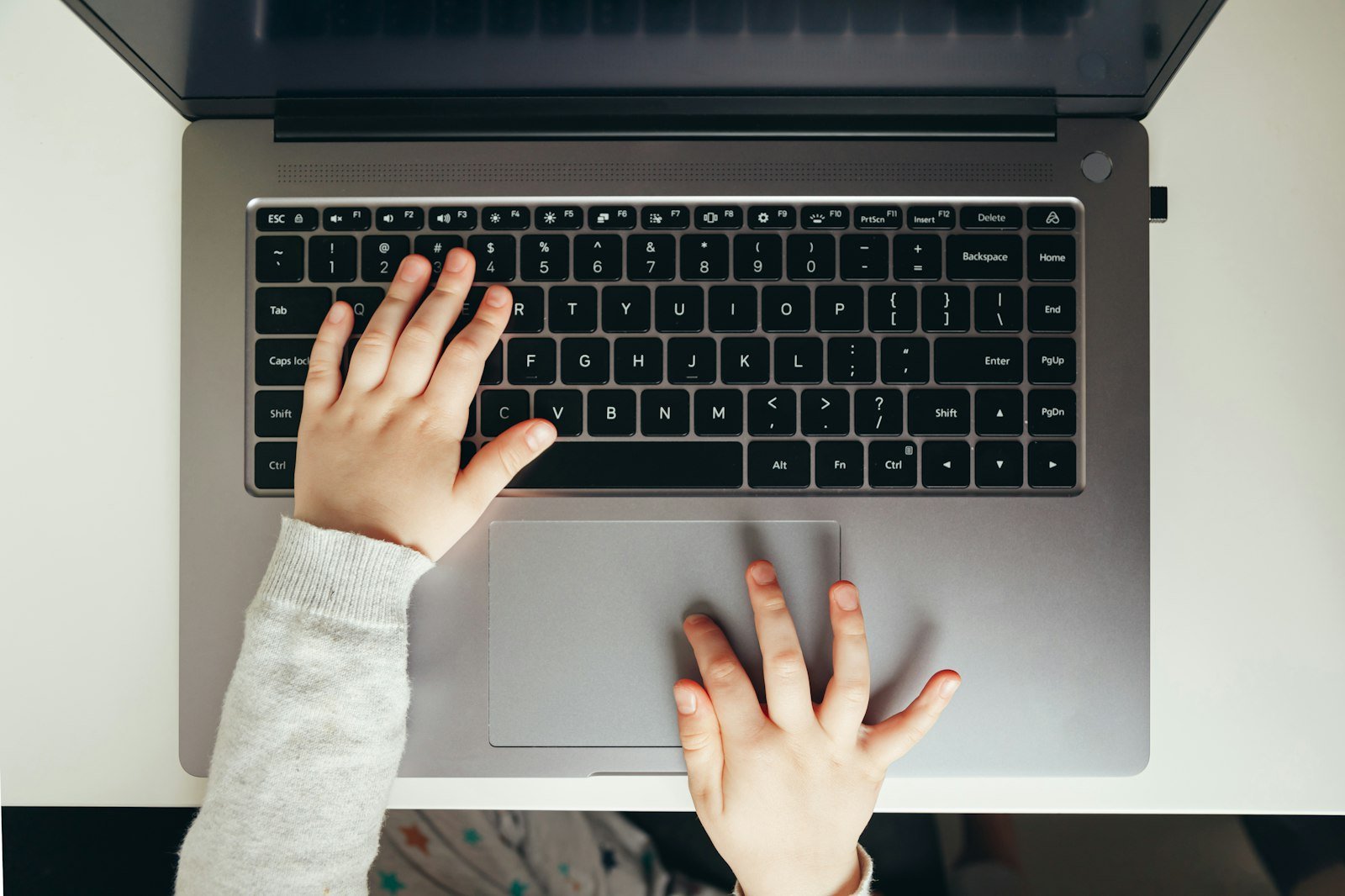 Close-up of a child's hands typing on a laptop keyboard