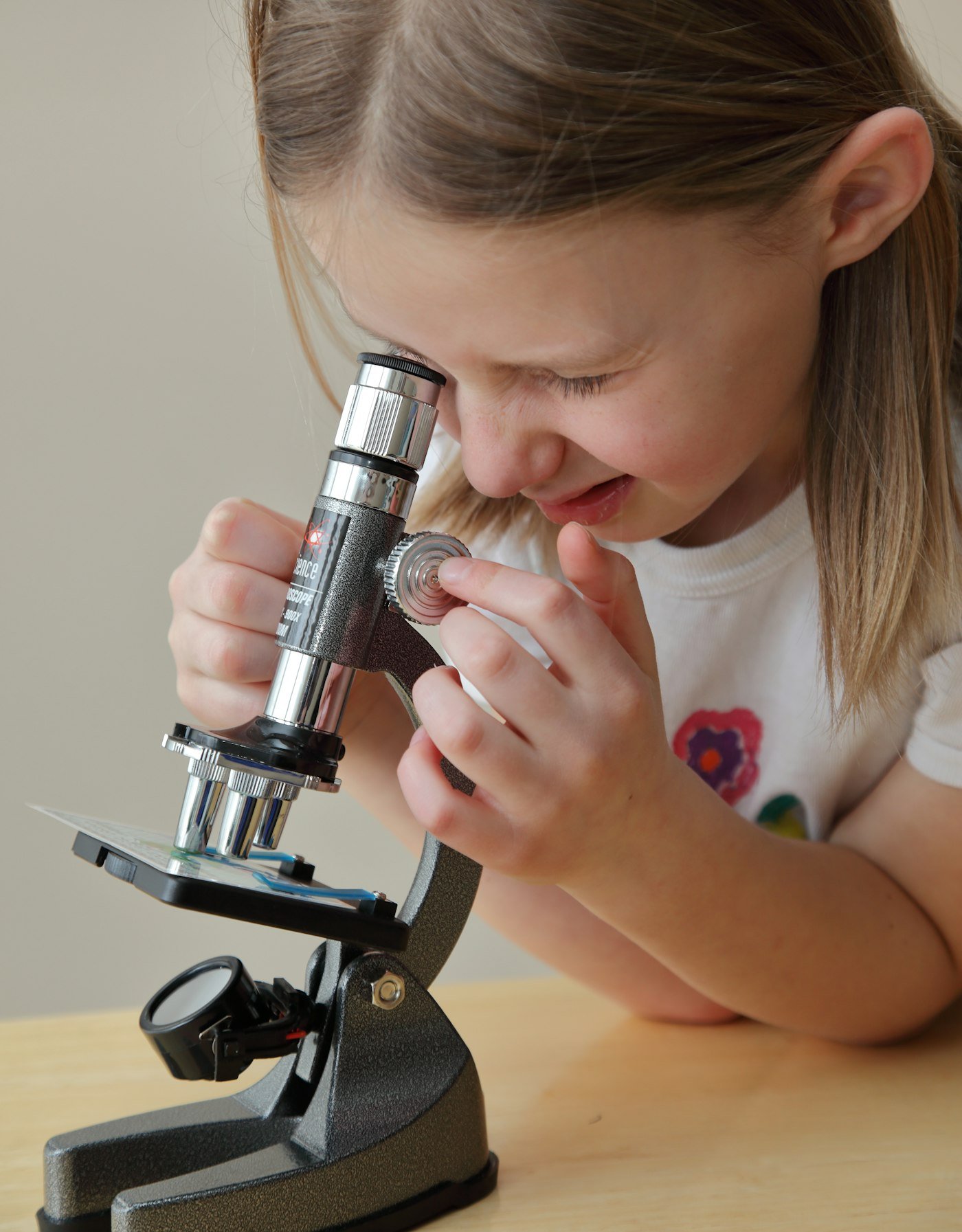 A young girl looks into a microscope, adjusting the focus