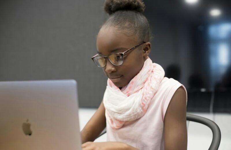 A young girl in glasses concentrating on a coding project on a laptop