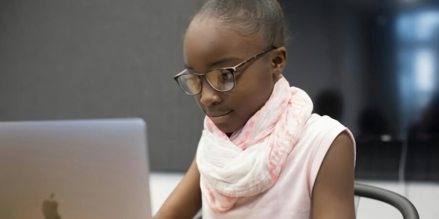 A young girl in glasses concentrating on a coding project on a laptop