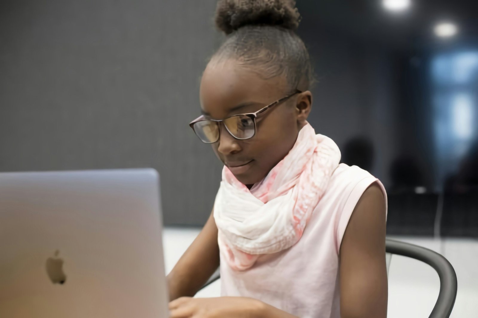 A young girl in glasses concentrating on a coding project on a laptop